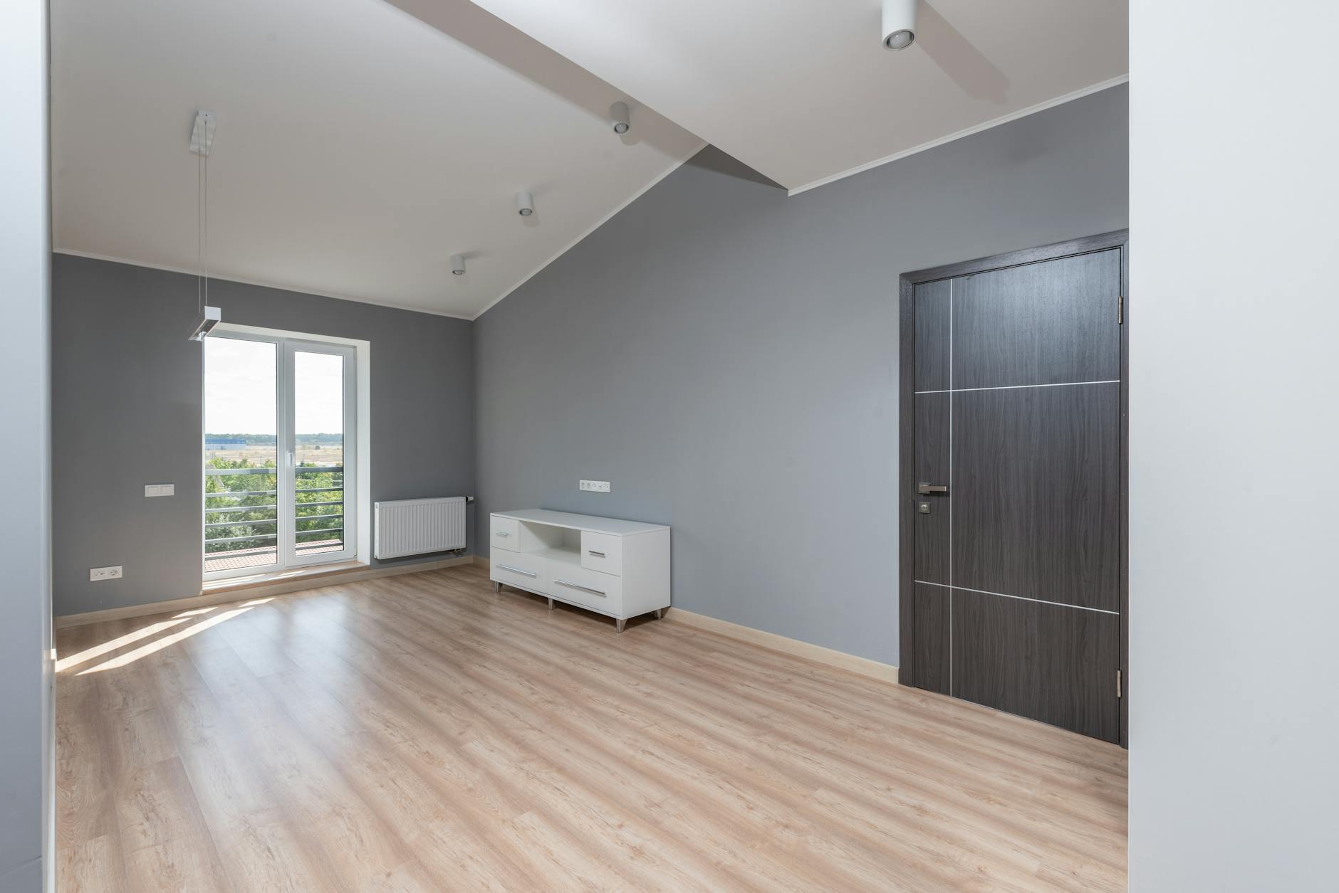 Jasny pusty salon z dużym oknem i drewnianą podłogą