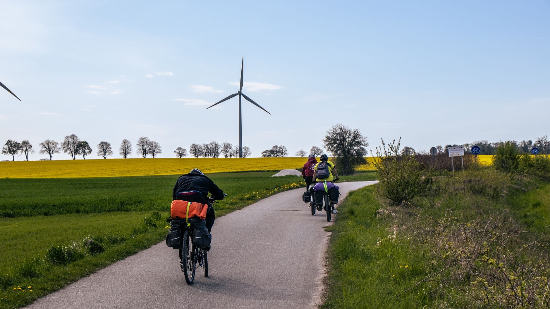 Rowerzyści na wiejskiej ścieżce wśród pól rzepaku i turbin wiatrowych